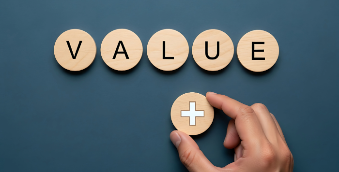 「VALUE」の文字が並んだ木製コインと、プラス記号のコインを置く手元。自社の価値向上をイメージした画像