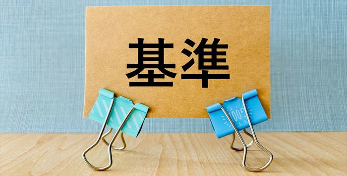 「基準」と大きく書かれた紙を4つのクリップで挟んだ画像。副業で個人事業主になるかどうかの判断基準を表すイメージ